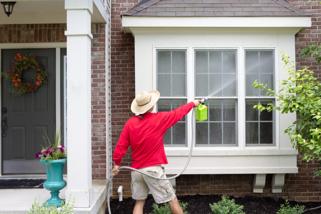 Technician performing roof & house washing on stucco and siding surfaces